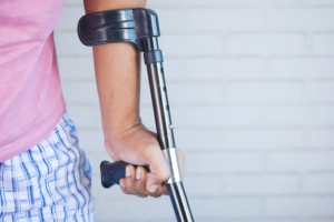 Close-up of a person in a pink shirt using a crutch for support indoors against a brick wall.